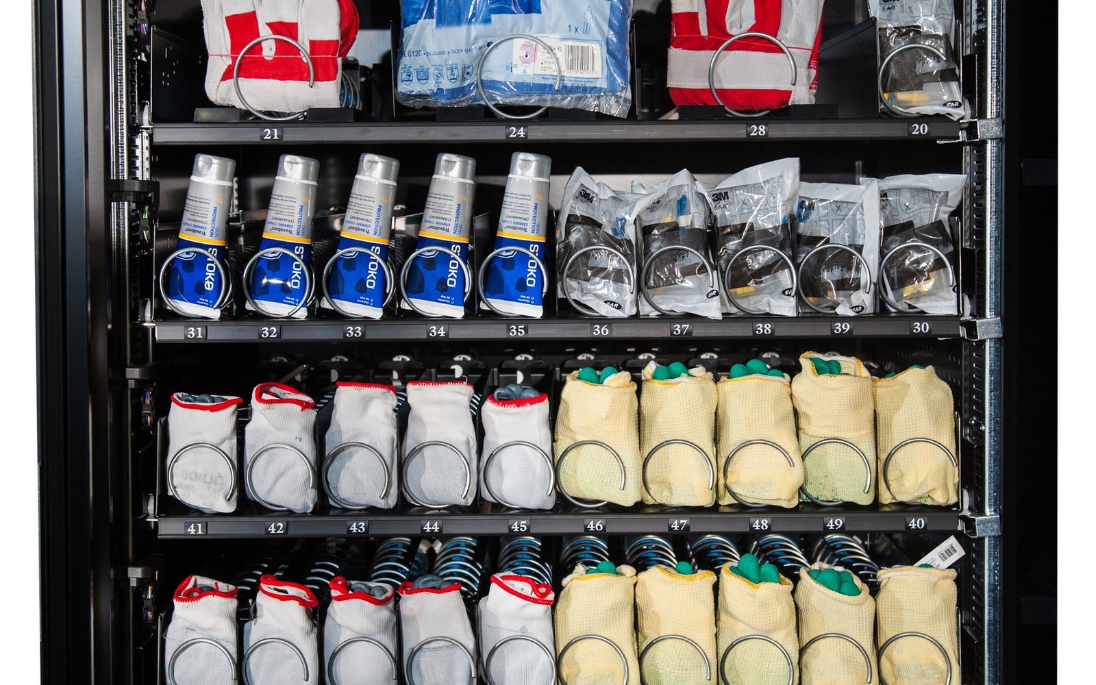 Interiorul unui automat de vending industrial OptiVEND, cu mănuși și echipamente de protecție pe spirale numerotate